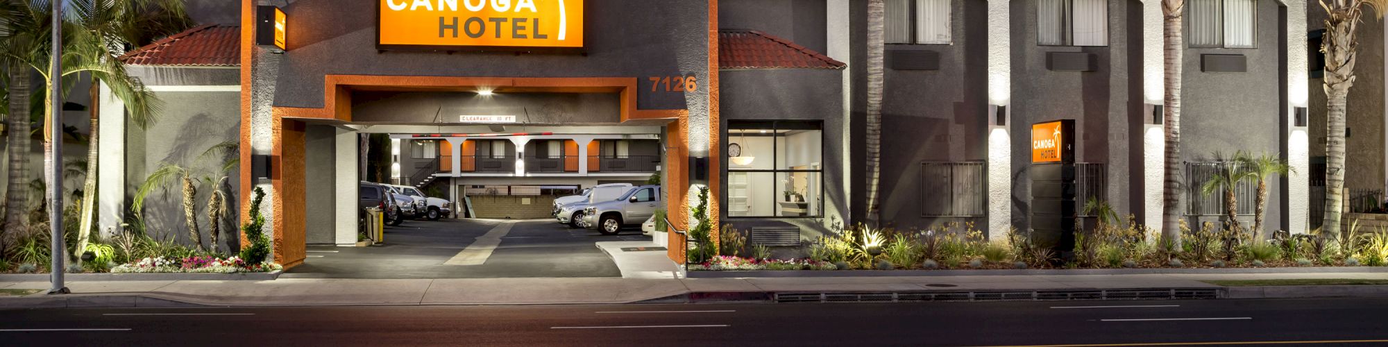 The image shows the front view of Canoga Hotel at night with lit signs, palm trees, and parked cars.