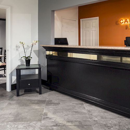 This image shows the reception area of Canoga Hotel, featuring a check-in desk, a seating area, and a potted orchid on a small table.