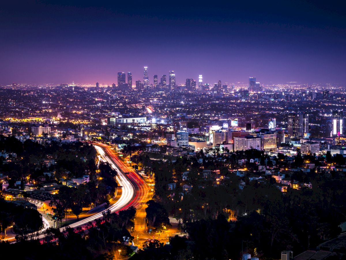 A cityscape at night featuring a brightly lit urban skyline with a winding road leading into the city, capturing the vibrant lights.