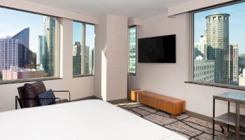 A modern bedroom with large windows offering a city view, minimalistic furniture, a wall-mounted TV, and a cozy chair near the window ends the sentence.