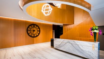 This image shows a modern reception area with a large clock, a marble desk, and an elegant spiral staircase.