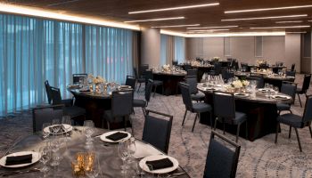 A banquet hall is set up with round tables, each adorned with elegant place settings, floral centerpieces, and black napkins, ready for an event.