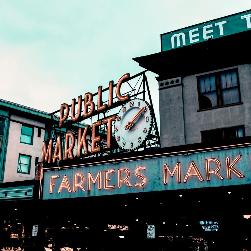 The image shows the entrance to a "Public Market" and a "Farmers Market" with neon signs and a clock, likely at a famous market location.