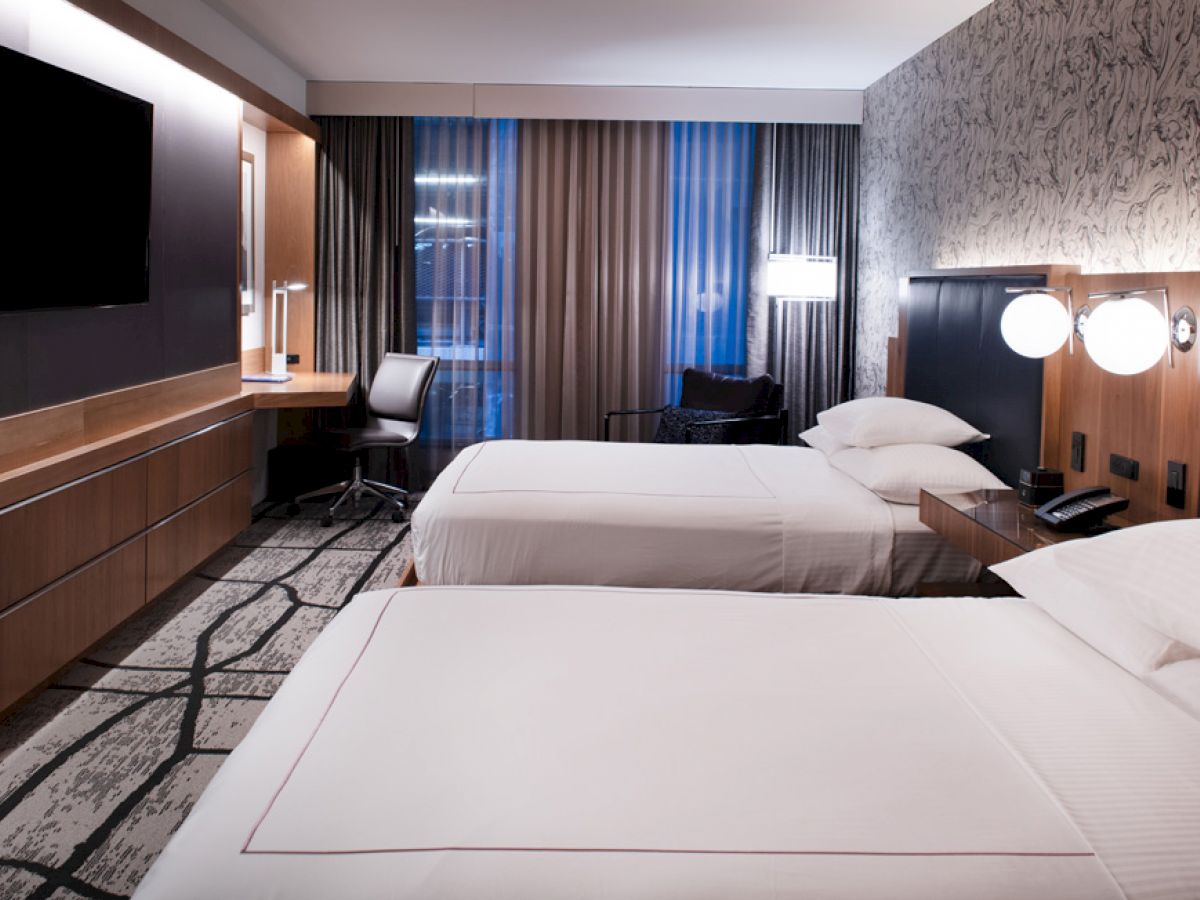 This image shows a modern hotel room with two neatly made beds, a wall-mounted TV, a desk, and a patterned accent wall behind the beds.