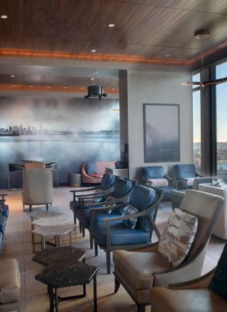 A modern lounge area with comfortable seating, stylish decor, large windows offering a scenic view, and a wall mural of a city skyline.
