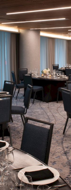 A banquet hall with round tables is elegantly set with plates, glasses, black napkins, and floral centerpieces, ready for a formal event.