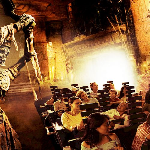 People are seated on a theme park ride with an animatronic skeleton holding a weapon in an ancient temple setting.